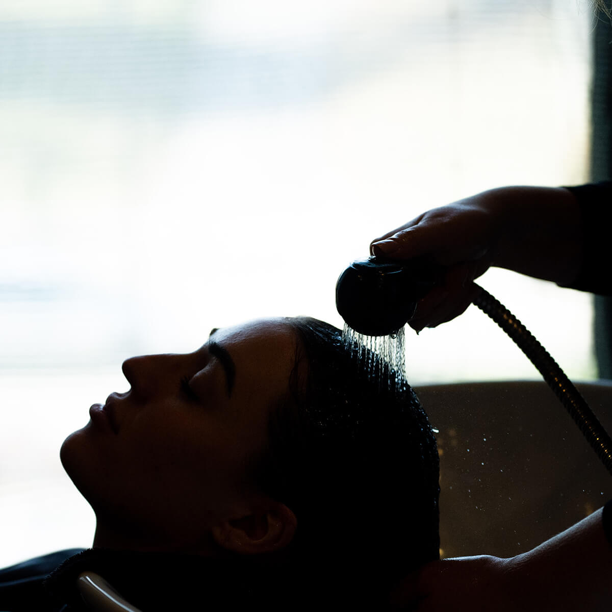 Silhouette of a person getting their hair washed at a luxurious spa salon with water pouring from a handheld showerhead.